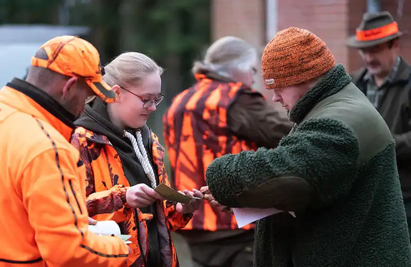 Jäger in leuchtend orangefarbenen Sicherheitswesten und Winterkleidung, die ein Gewehr untersuchen.