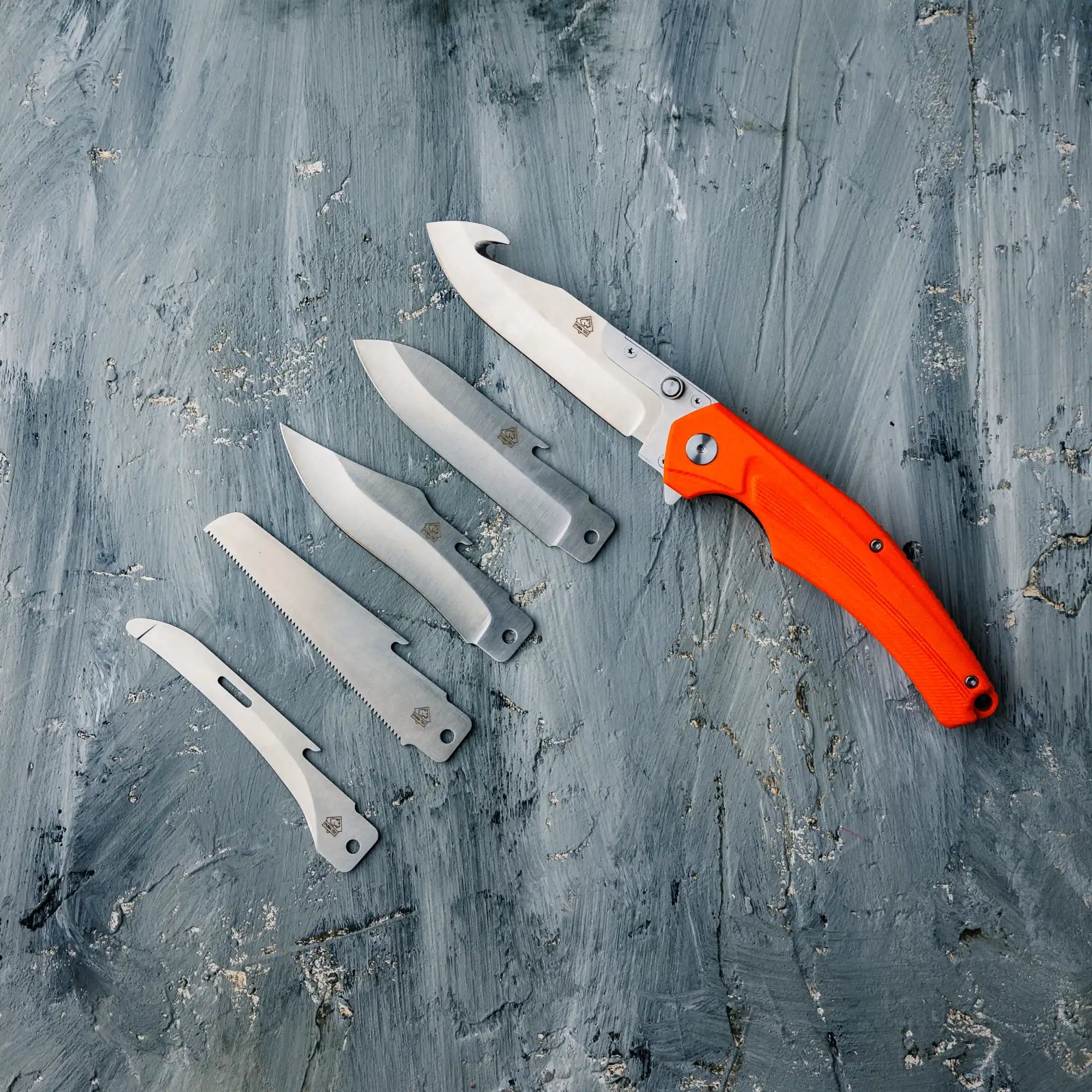 Sammlung von Klapp-Taschenmessern mit einem Messer mit orangefarbenem Griff.